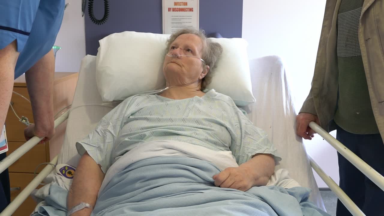 Elderly female patient listening to nursing staff explain health concerns while husband listens. Captured in medical ward setting