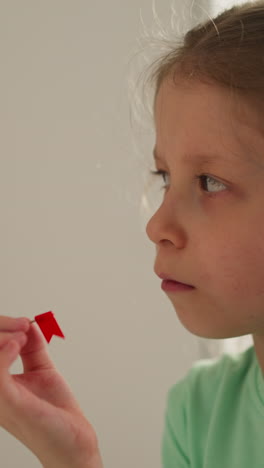 schoolgirl spins pin with red flag in hand and looks aside thoughtfully. calm kid ponders over study tasks sitting in light premise. education in primary school closeup