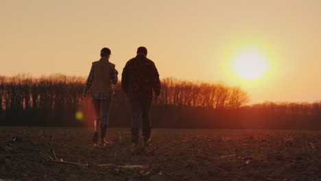 two farmers a man and a woman walking along a plowed field talking