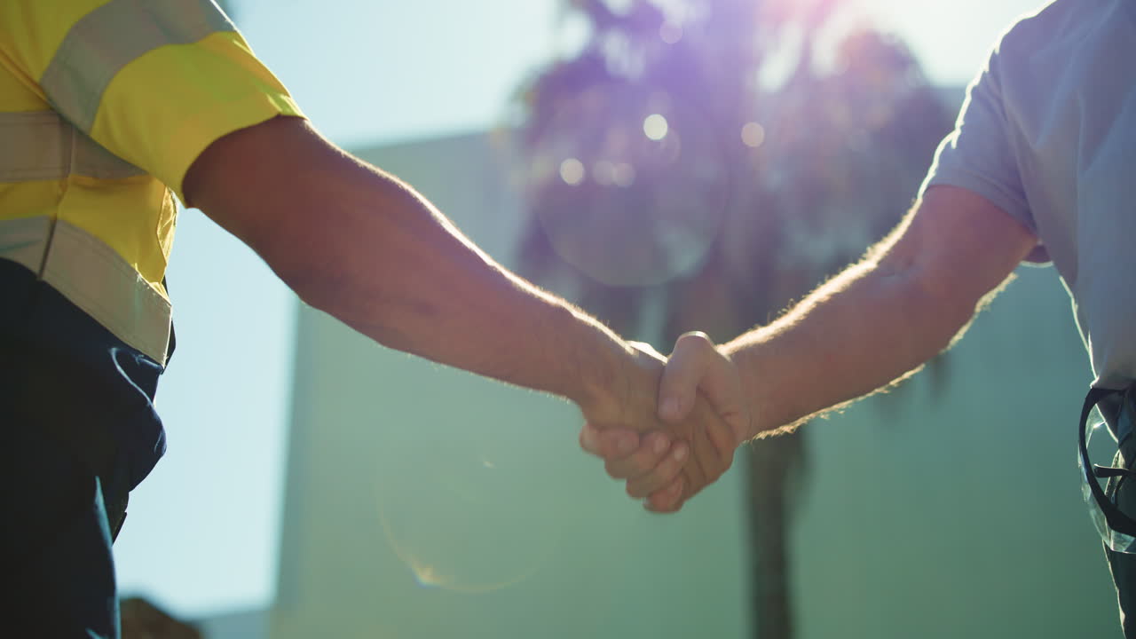 Two Workers Shaking Hands Outdoors in Bright Sunlight