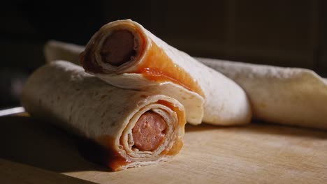 a close up shot of a complete tortilla hotdog, a grilled frankfurter sausage wrapped in a wheat tortilla neatly presented on a wooden cutting board