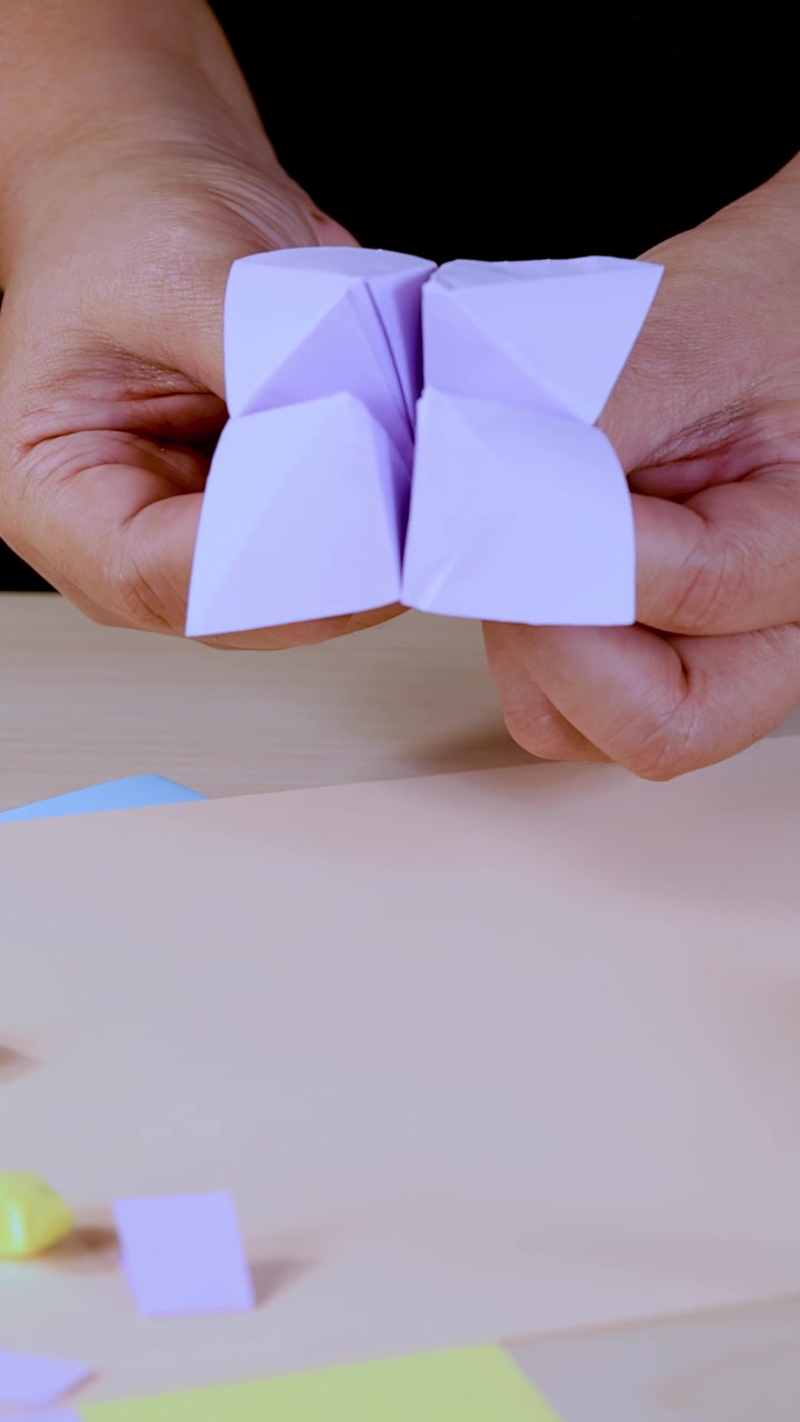Mani adulte manovrano un indovino di carta origami sotto una luce soffusa, primo piano, sfondo neutro