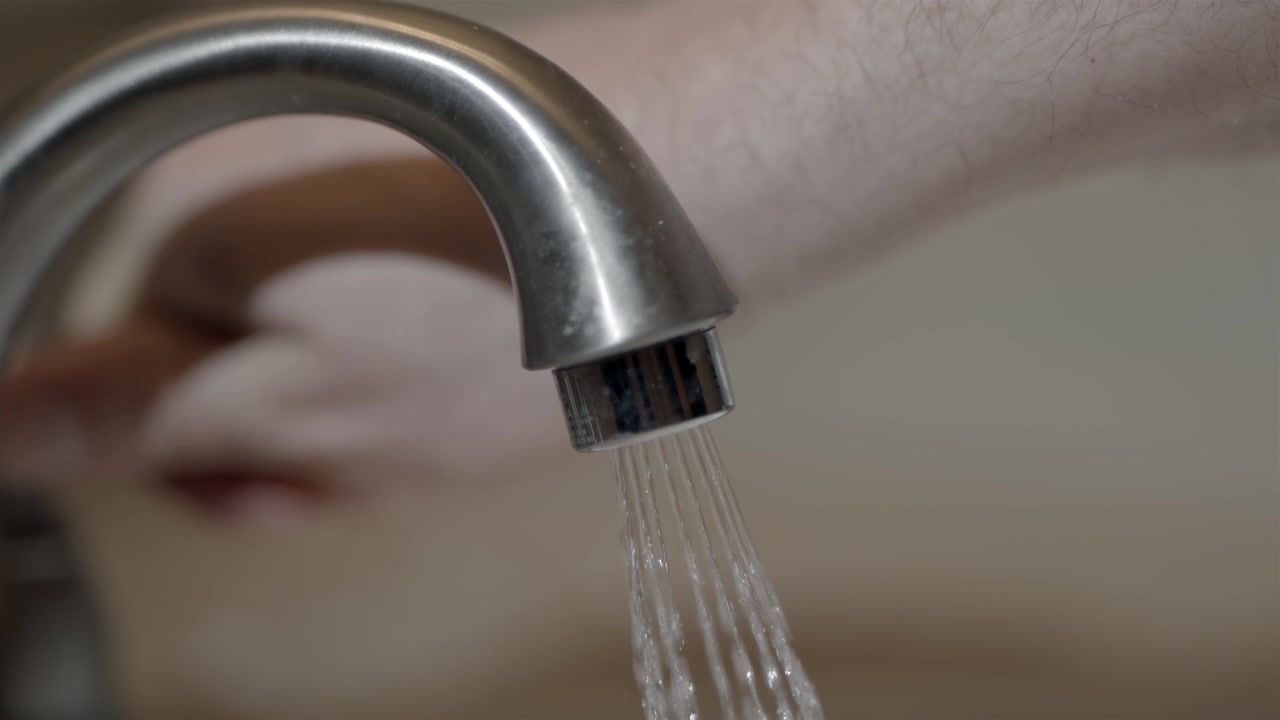Macro shot of running water from chrome faucet during domestic chores