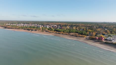 Aerial-view-of-the-coast-of-the-Baltic-Sea,-the-rippling-sea,-a-sandy-beach,-a-nearby-forest,-and-private-houses-built-in-it