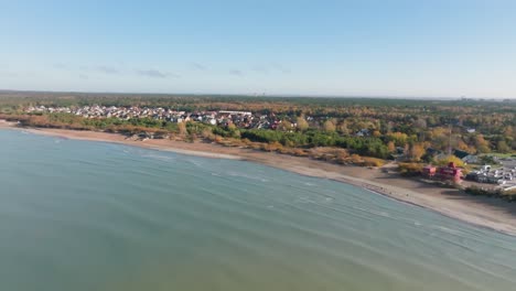 vista aérea de la costa del mar báltico, el mar ondulante, una playa de arena, un bosque cercano y casas privadas construidas en él