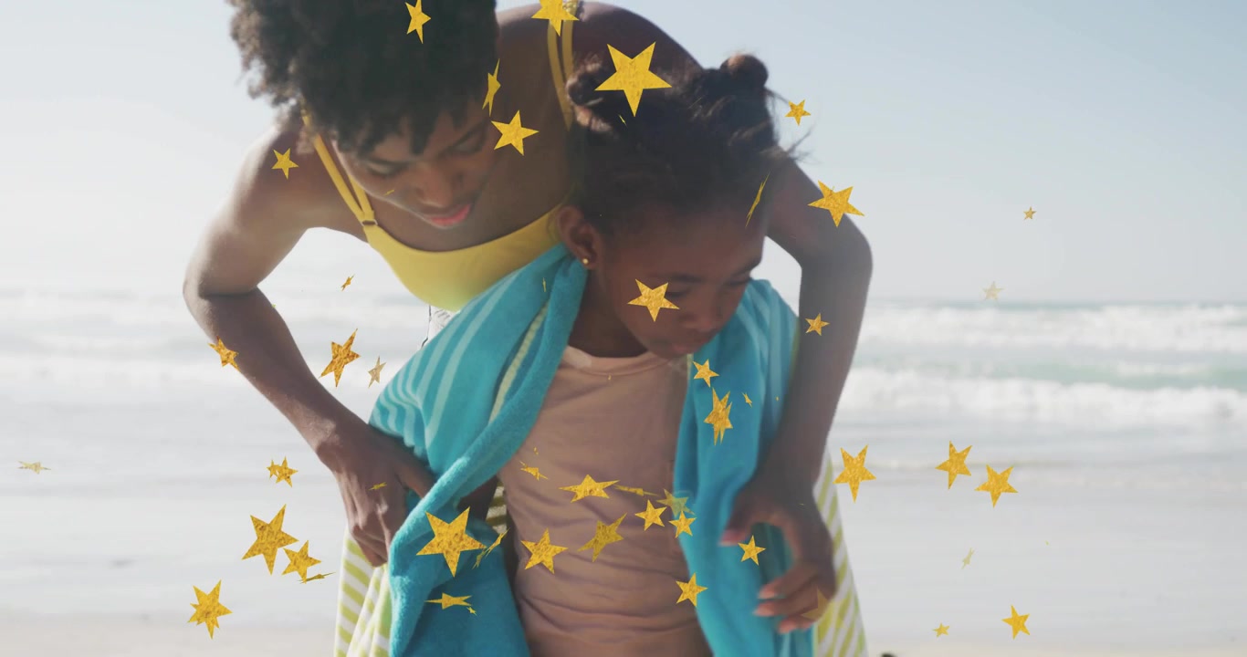 Mãe colocando uma toalha azul na criança na praia, envolvendo a família para secar, com estrelas douradas cobrindo parcialmente os rostos.