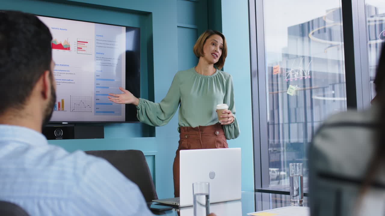 Presenting in meeting room, woman holding coffee cup and speaking to colleagues