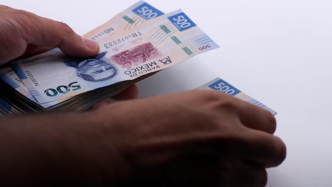 Detailní záběr muže počítajícího mexické pesos. Ateliérový snímek