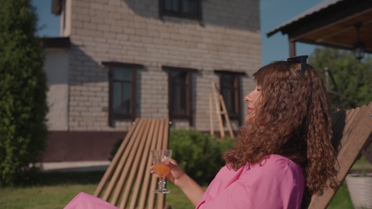 Elegant Woman With Sunglasses In Garden Setting, Relaxed Female Figure With Curly Hair And Cocktail Outdoors, Stylish Woman With Curly Locks Adjusting Sunglasses In Tranquil Suburban Garden Scene