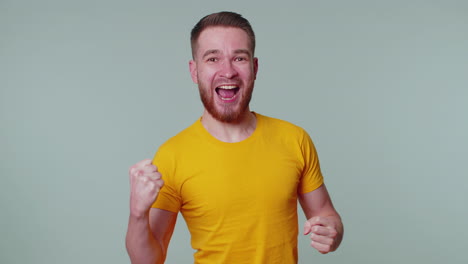 stylish man in t-shirt shouting, raising fists in gesture i did it, celebrating success, winning