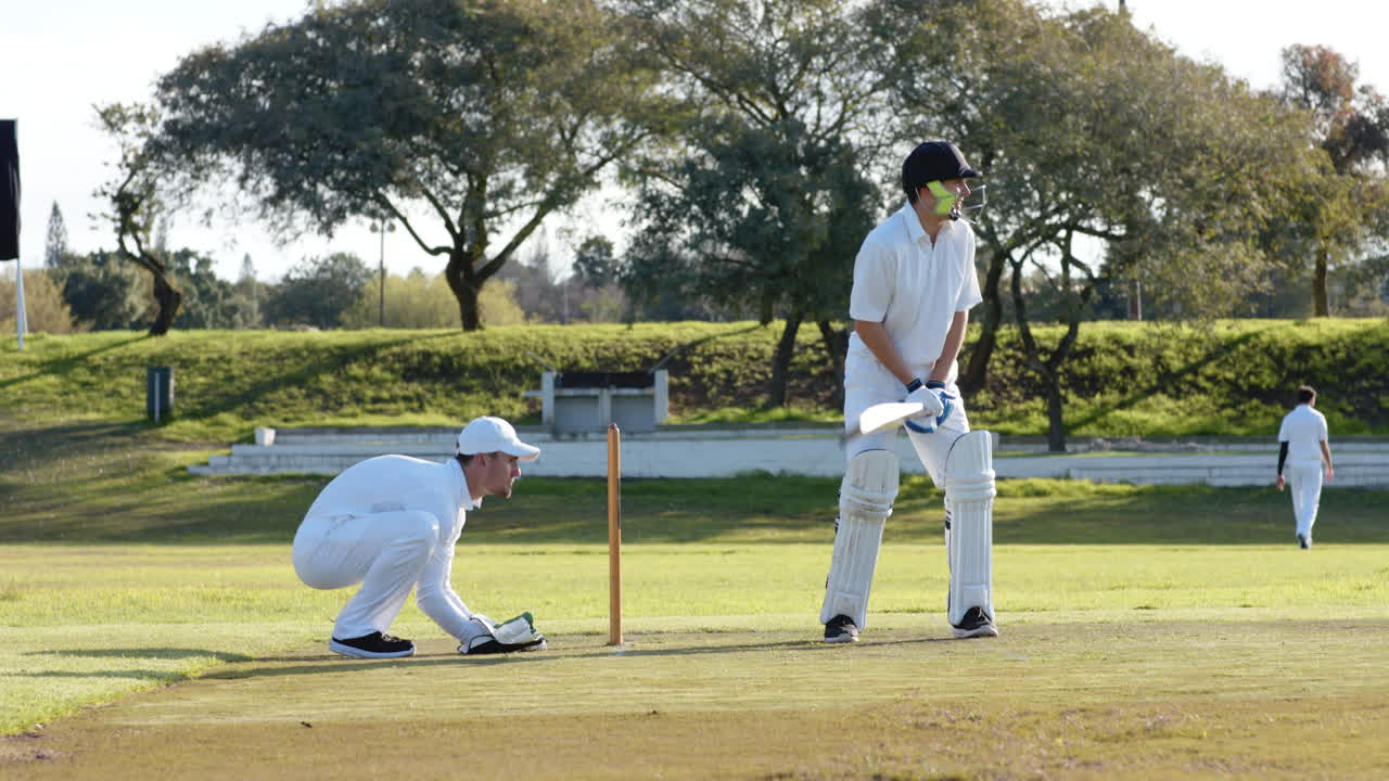 Two teams of multiracial male cricket players playing cricket, batter hitting ball on pitch