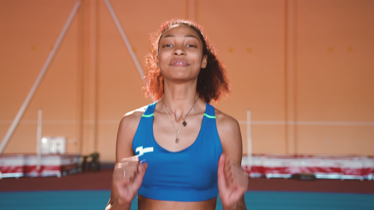 emocionada deportista saltando y animando para celebrar la victoria mientras mira la cámara en una instalación deportiva cubierta