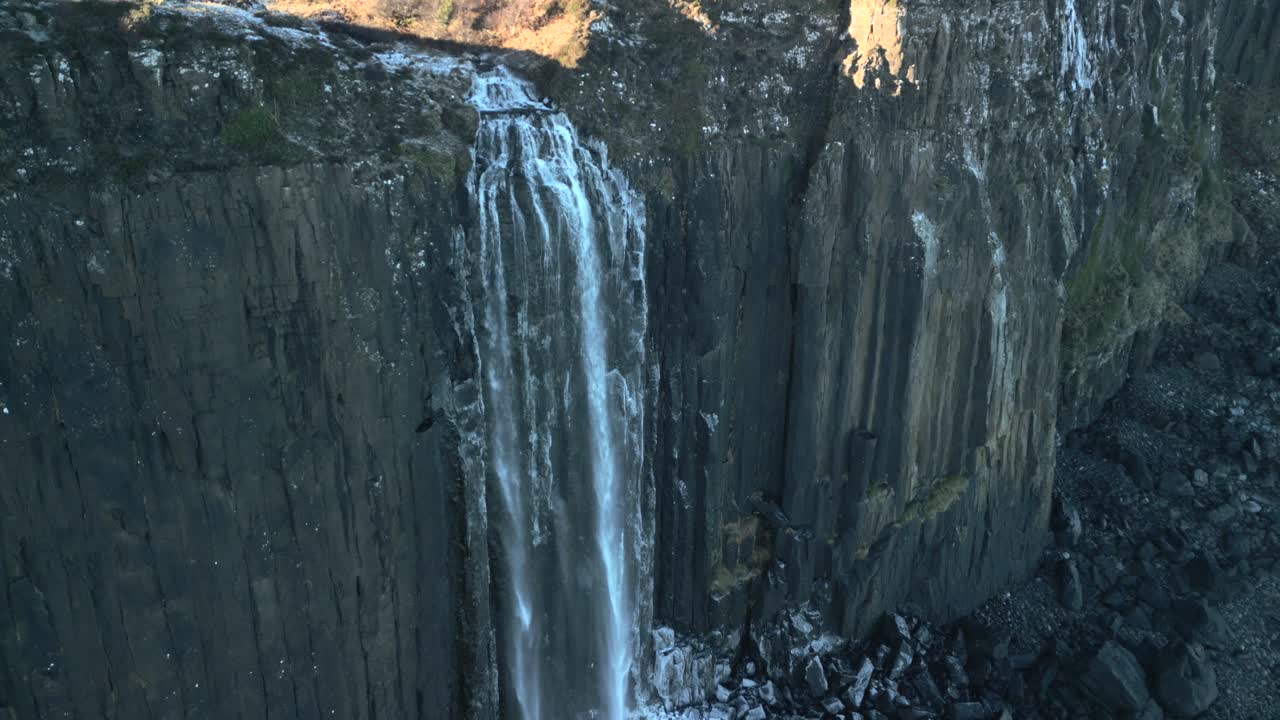 cascada media velocidad órbita de movimiento lento en la sombra cayendo por un acantilado escarpado a la playa rocosa helada debajo en invierno en cascada de kilt rock, isla de skye, tierras altas occidentales, escocia, reino unido