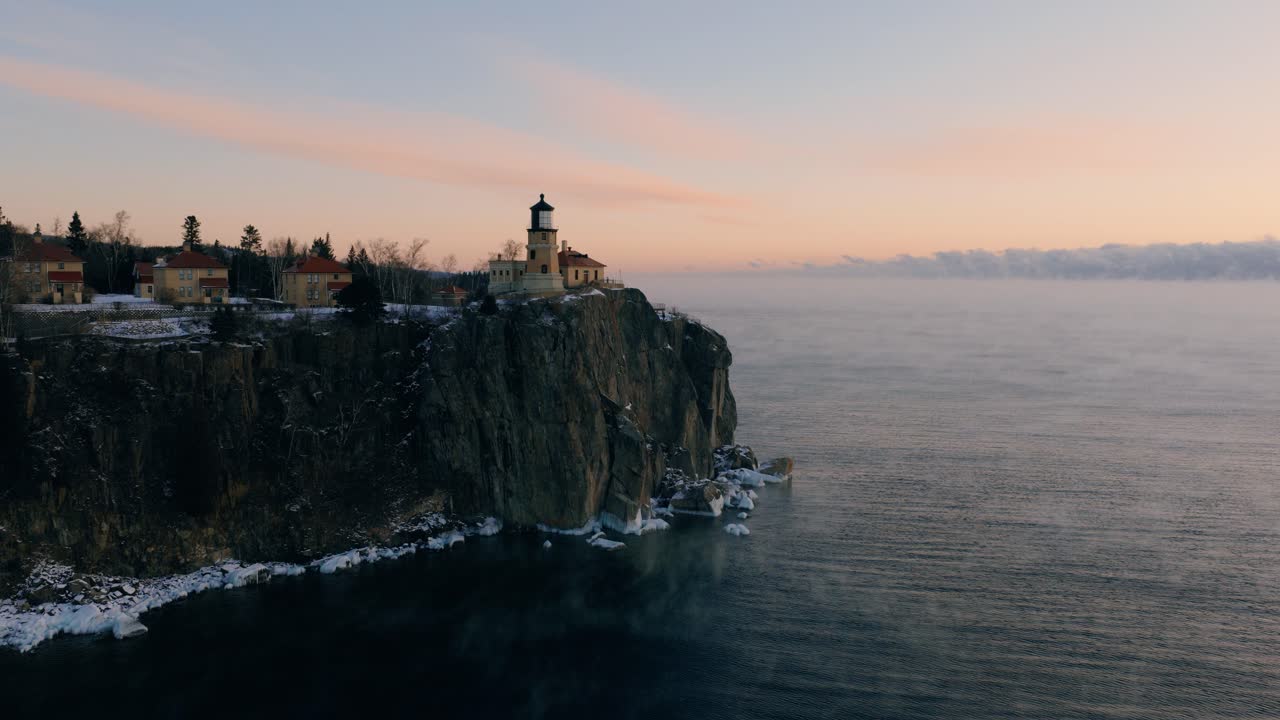 High-angle aerial looking down at the lighthouse and icy cliffs, showcasing the dramatic winter landscape of Lake Superior's North Shore