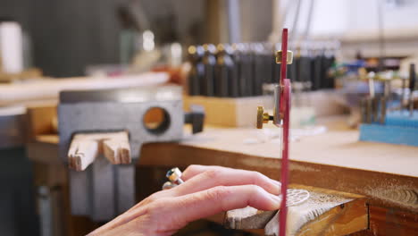 close up of female jeweller working on brooch with saw in studio