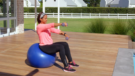 Mixed-race-mature-woman-exercising-with-dumbbells-at-backyard-on-a-sunny-day-4k