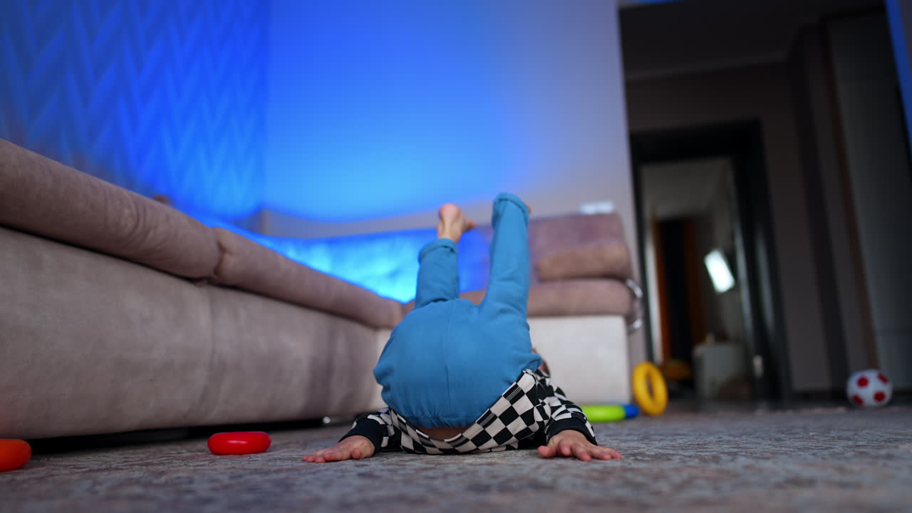 Cheerful baby boy plays on the floor raising his legs. Active toddler having fun time at home.