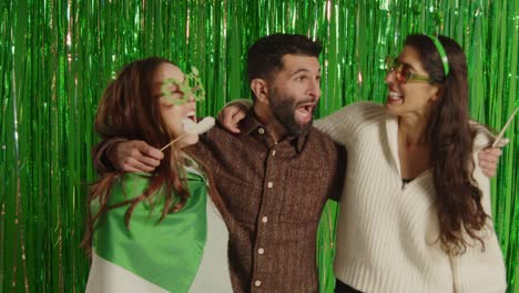 retrato de estudio de amigos vestidos con novedades irlandesas y accesorios celebrando el día de san patricio contra un fondo de oropel verde 1