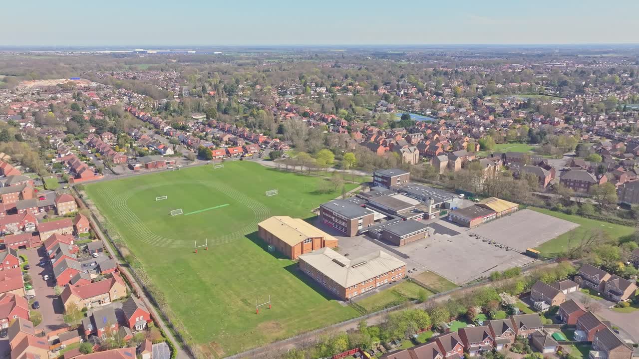 Aerial static shot of Doncaster Lakeside showing a large school campus with open sports field, nearby residential houses and green suburban landscape under clear spring sky