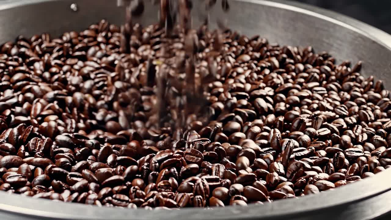 Il video cattura chicchi di caffè che cadono a cascata in un contenitore di metallo, enfatizzando texture ricche.