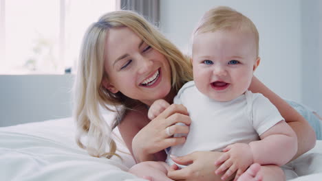 mother lying on bed at home gives baby son kiss