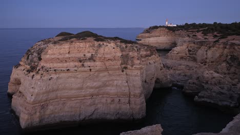 Der-Leuchtturm-Farol-De-Alfanzina-Blitzt-Kurz-Vor-Sonnenaufgang-Auf-Einer-Klippenspitze-Der-Algarve-Mit-Der-Halbinsel-Cabo-Carvoeiro-Im-Vordergrund-Auf