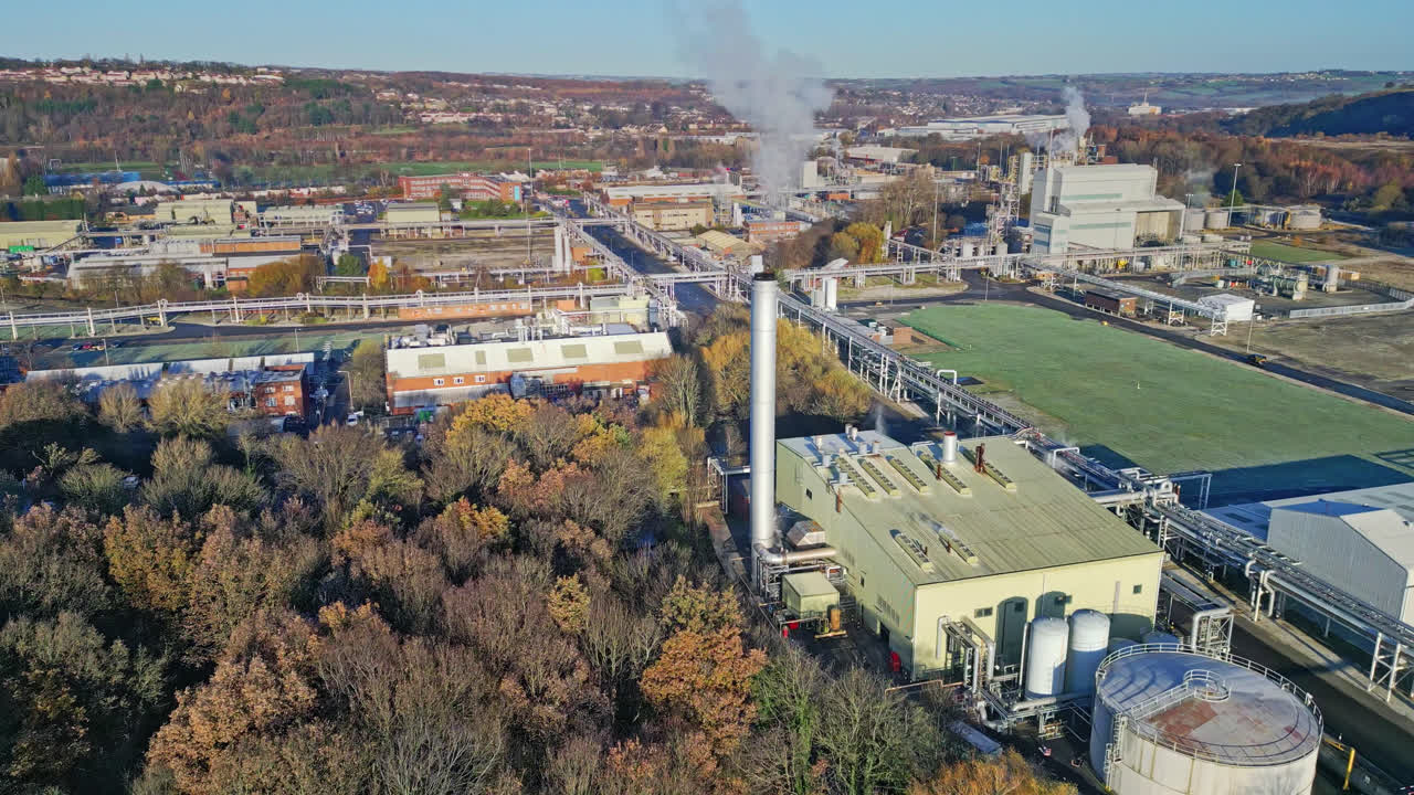 Aerial footage moving towards a large industrial chemical plant, showing pipelines, metal structures, cooling towers and chemical storage