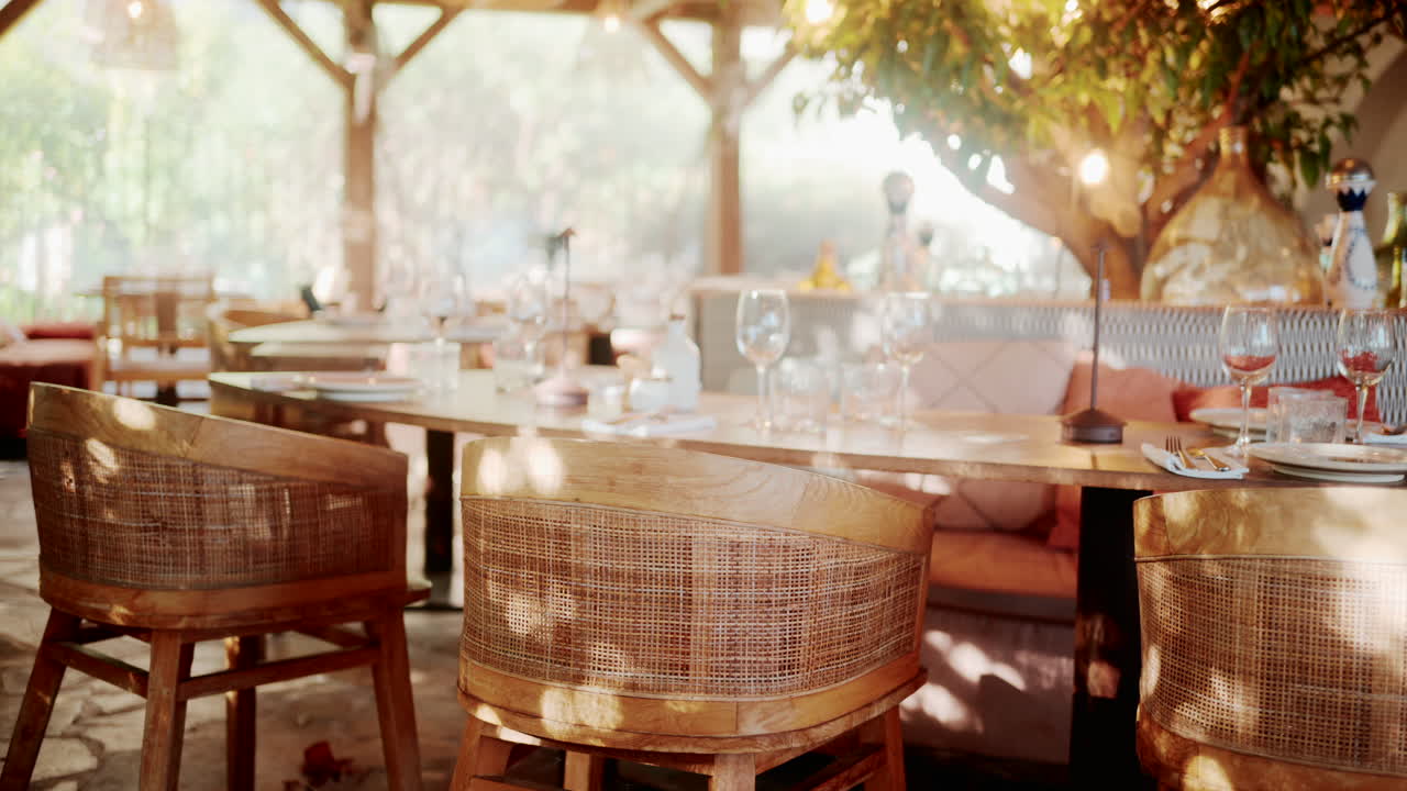 Wooden restaurant table prepared with glasses, plates, and napkins in warm natural light