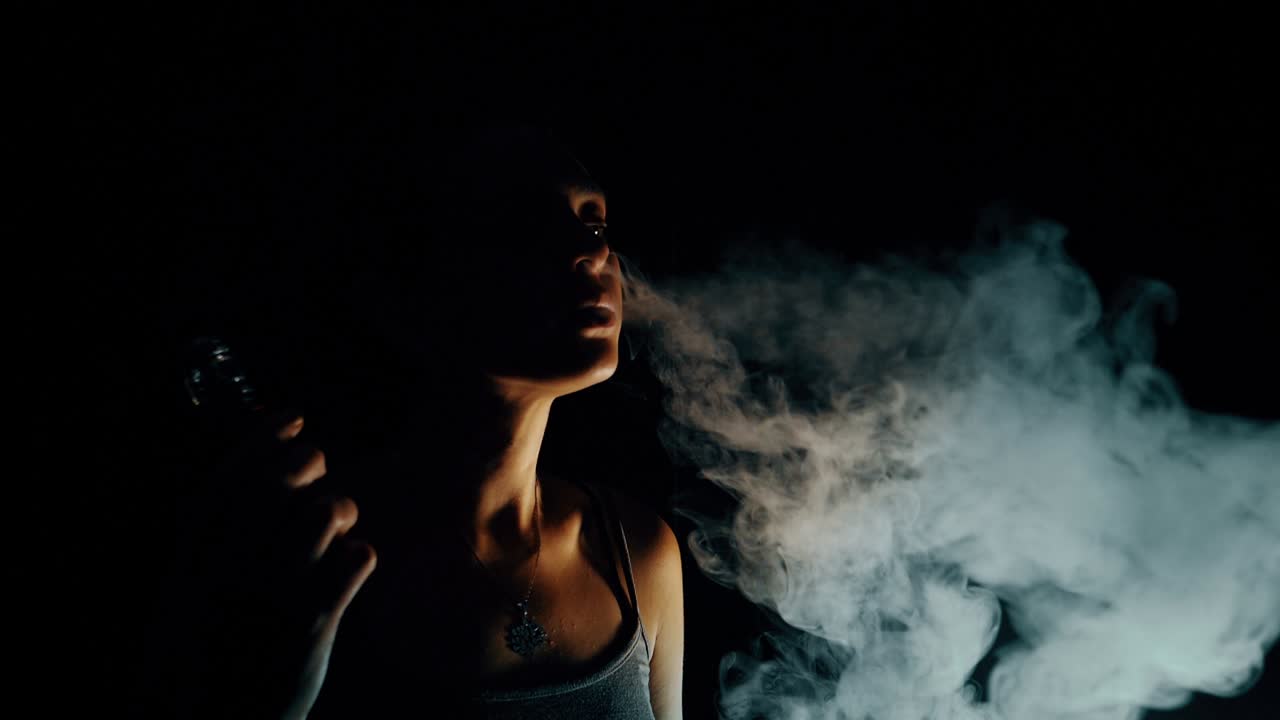 Young Woman Vaping and Exhaling Large Cloud of Smoke in Dark Room