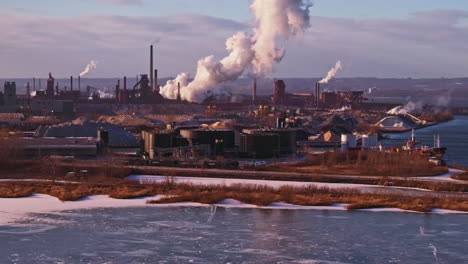 Winterliche-Industrielandschaft-Mit-Schornsteinen-Und-Zugefrorenem-Fluss,-Licht-Am-Späten-Nachmittag,-Weitwinkelaufnahme