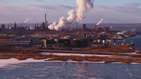 winter industrial landscape with smokestacks and frozen river, late afternoon light, wide shot