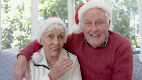 una pareja caucásica mayor con sombreros de papá noel haciendo una llamada de video de navidad, en cámara lenta.