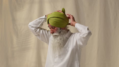 une photo de studio d'un homme sikh âgé avec une barbe liant un tissu pour un turban sur un fond plat 3