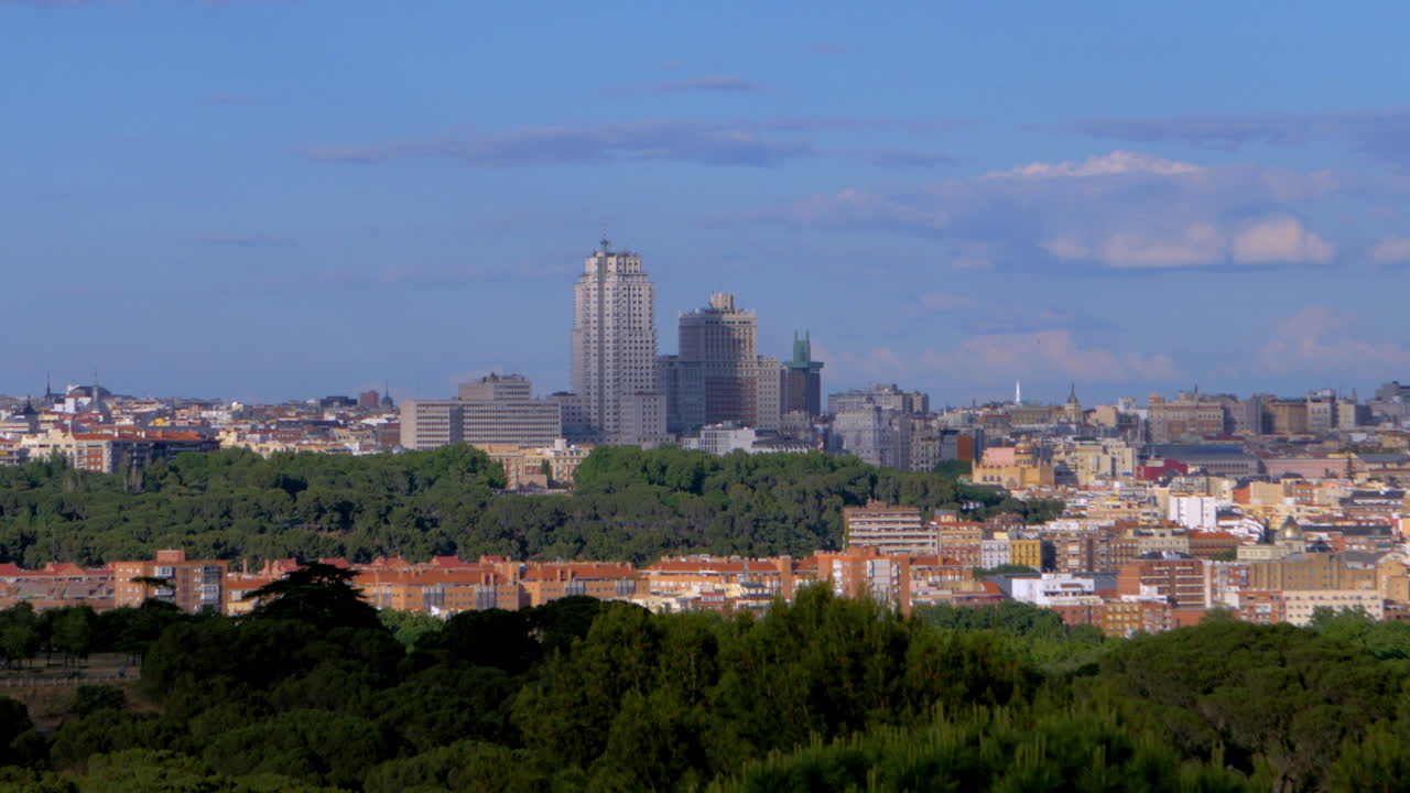 Madrid’s skyline emerges from a sea of trees, where classic rooftops meet modern towers under a soft blue afternoon sky.