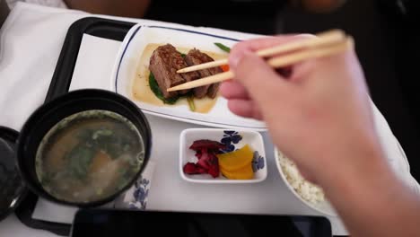 person eating steak, vegetables, rice, and miso soup