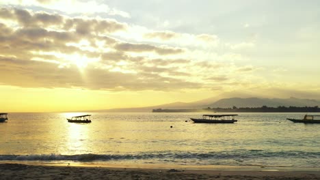 Bright-sky-with-beautiful-clouds-hanging-over-calm-sea-surface-reflecting-yellow-colors-of-romantic-sunset,-anchored-boats-on-bay,-Bali