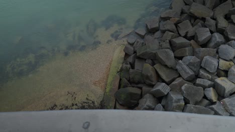 Waves-crash-into-rocks-and-pebbles-on-a-small-secluded-beach,-bird's-eye-view