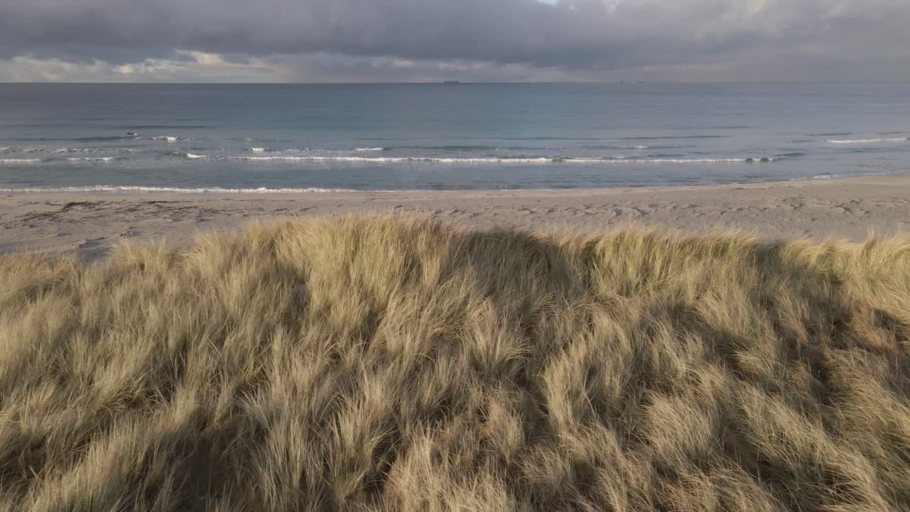 전경에 장엄한 모래 언덕이 있는 바다 위의 폭풍우 구름, 공중 측면 플라이 샷