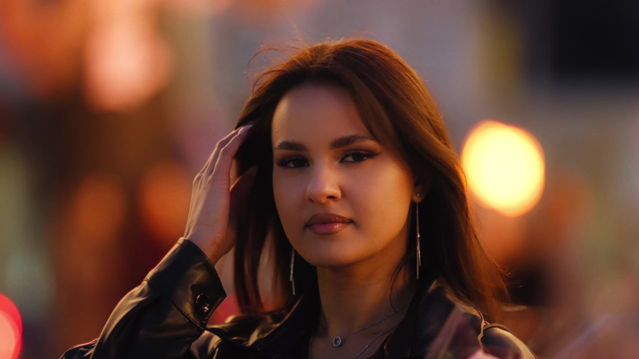 Ritratto di una bella ed elegante giovane donna che si passa una mano tra i capelli, in una città affollata, di notte