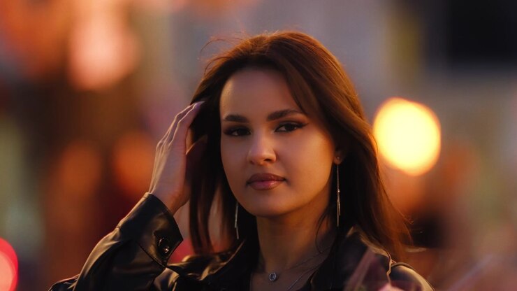 Ritratto di una bella ed elegante giovane donna che si passa una mano tra i capelli, in una città affollata, di notte