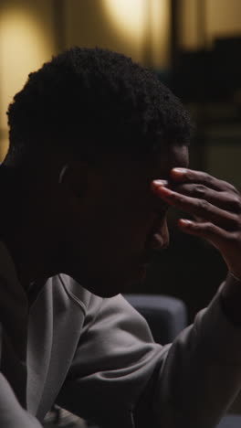 vertical video close up of unhappy and depressed young man sitting on sofa at home looking anxious and worried resting head in hands 1