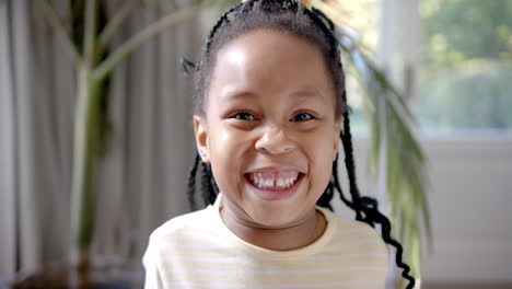 Retrato-De-Una-Feliz-Chica-Afroamericana-Con-El-Pelo-Trenzado-Sonriendo-Junto-A-Una-Ventana-Soleada,-Cámara-Lenta