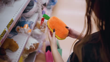 vista lateral de cerca de una mujer sosteniendo un elegante bolso de color naranja esponjoso con diseño de hoja verde, examinando detalles mientras hace compras, una compradora con uñas negras explora el pasillo de accesorios en una tienda minorista moderna