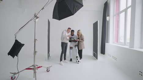 behind-the-scenes photo shoot: a photographer in a photo studio uses a flash for photos of a black professional football player. photo shoot in the studio of a sports magazine advertising