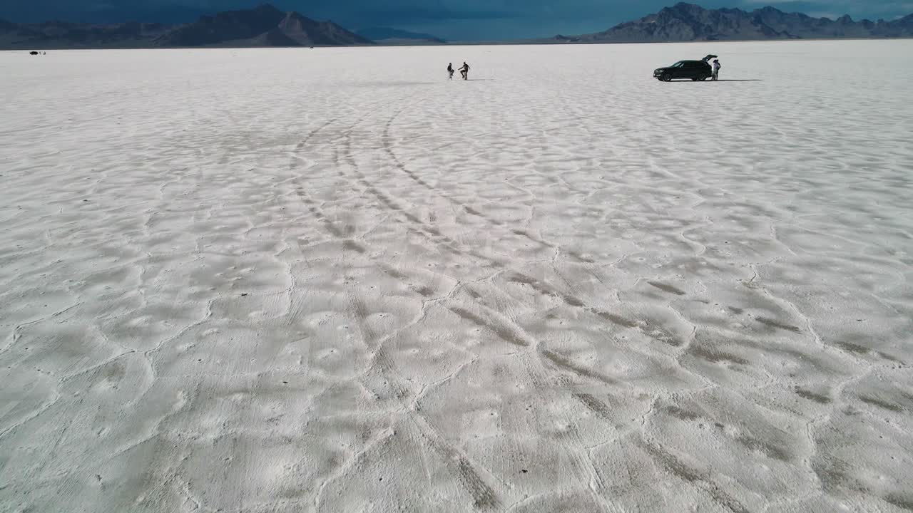 Cinematic high speed drone shot pulling out from two people sitting on chairs with unrecognizable faces at sunset in a epic remote location bonnesville salt flats, utah 4k aerial drone clip