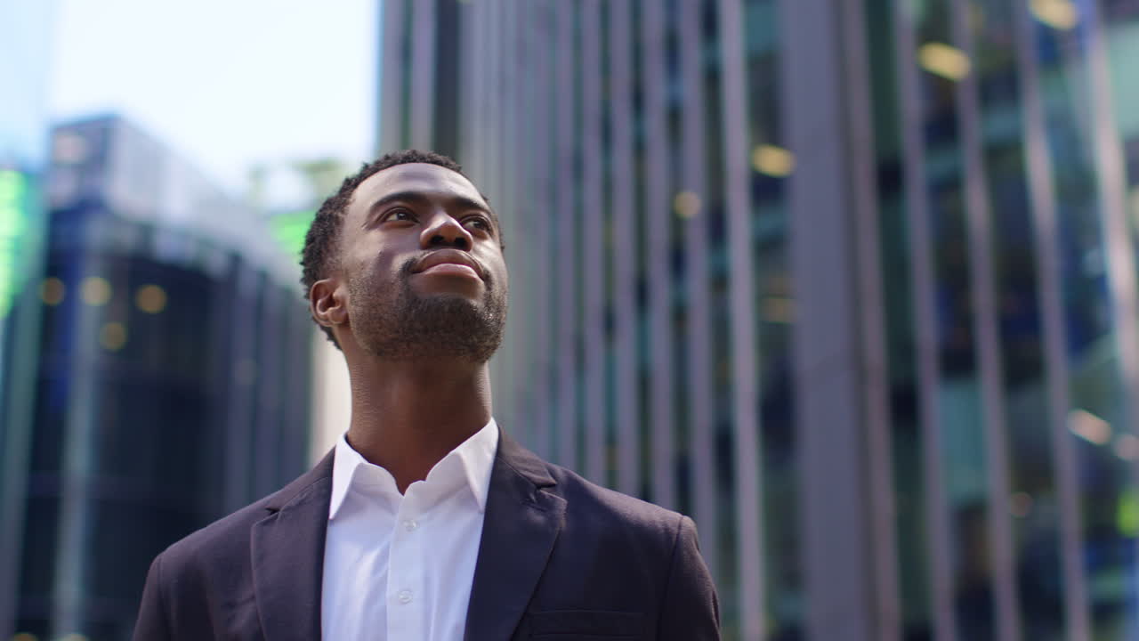 retrato de un joven empresario confiado que lleva un traje de pie afuera mirando hacia las oficinas en el distrito financiero de la ciudad de londres, reino unido.