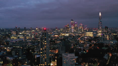 Volar-Sobre-La-Terraza-Superior-Del-Edificio-Residencial-De-Gran-Altura.-Reveladora-Vista-Panorámica-Del-Paisaje-Urbano-Nocturno-Con-Rascacielos-Del-Centro.-Londres,-Reino-Unido