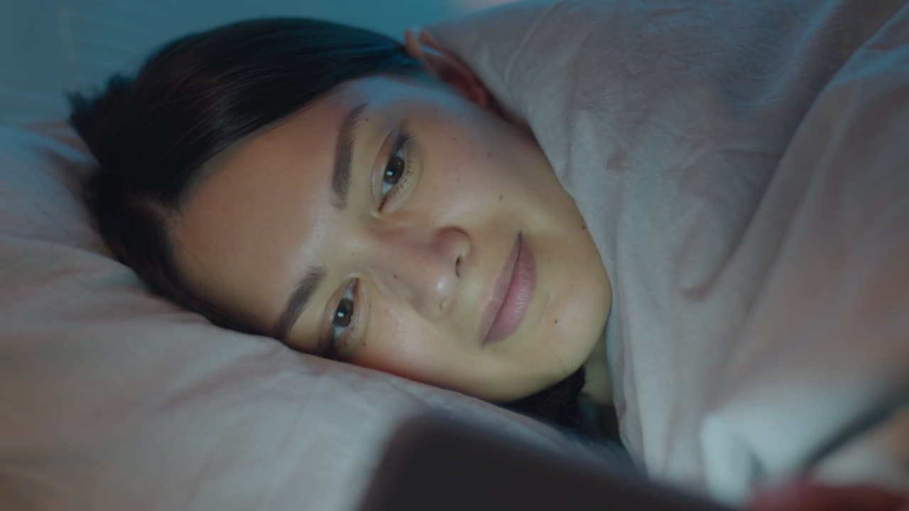 밤에 침대에서 스마트폰을 사용하는 여성