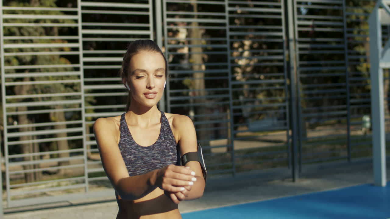 mujer deportiva con airpods calentando y estirando los brazos en la cancha deportiva en la mañana de verano