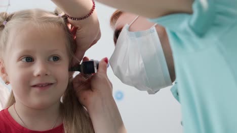 a pediatrician in a hospital checks the ear of a little girl.